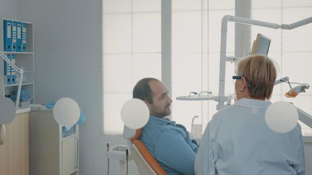 Patient with dental appointment arriving at stomatology cabinet, talking to mature dentist about oral care procedure. Man attending stomatological examination with specialist in cabinet.