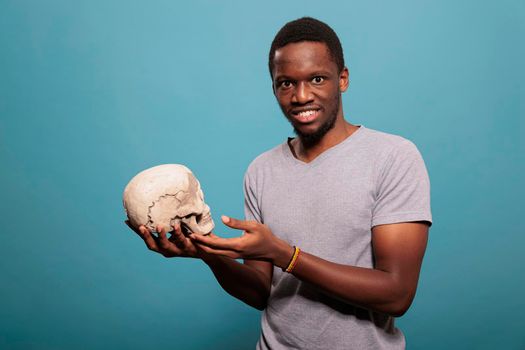 Smart man holding human skull to learn anatomical knowledge