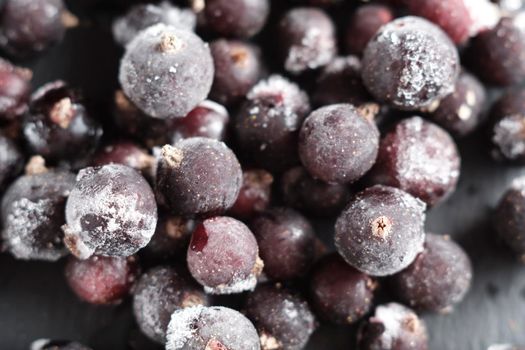 natural frozen blackcurrant berries covered with hoarfrost scattered on a slate dish.