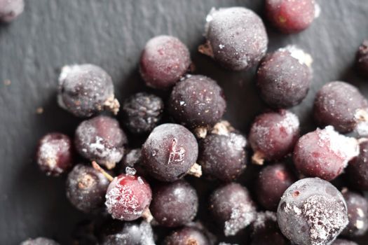 natural frozen blackcurrant berries covered with hoarfrost scattered on a slate dish.