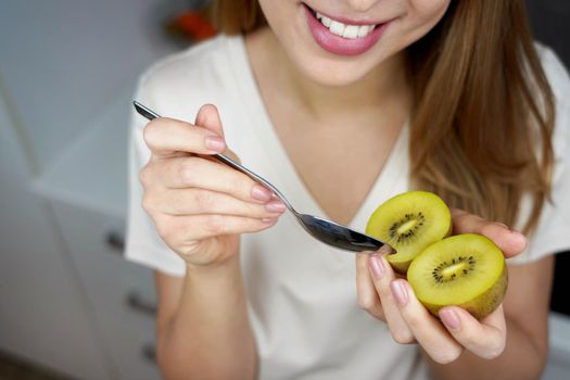 Happy young healthy woman eating a golden kiwi at home. Antioxidant, Vitamin C, healthy concept.