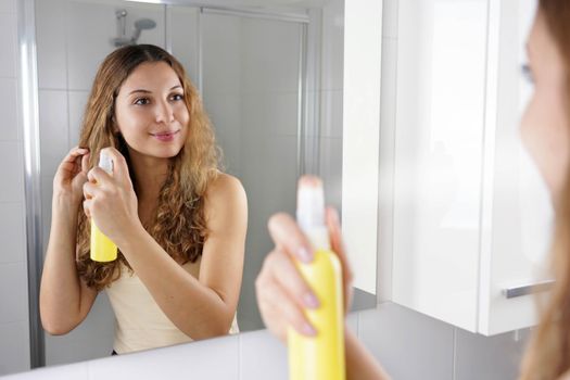 Hair lightening spray. Smiling girl applying hair lightening spray for dyeing hair. Haircare cosmetic.