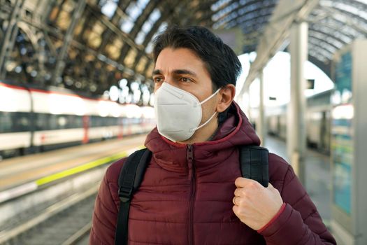 Portrait of traveler man wearing KN95 FFP2 medical face mask with moving train on background on train station