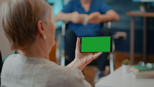 Female pensioner looking at horizontal green screen on mobile phone