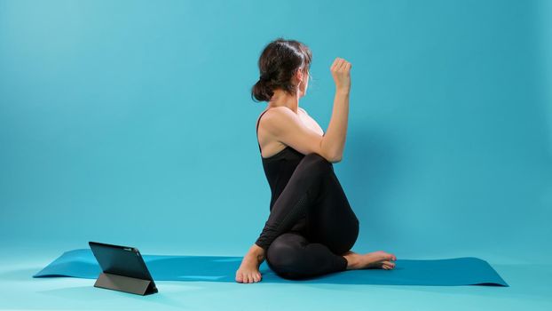 Fit adult following pilates lesson on tablet to stretch body