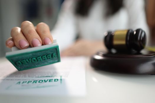 Hand puts stamp approved on document near judge's gavel