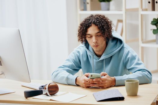 A young man in a blue jacket in front of a computer with phone Lifestyle