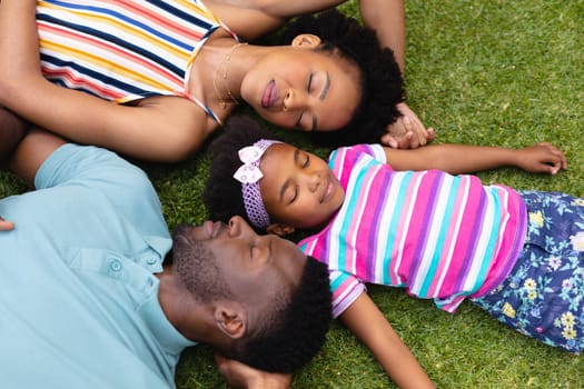 Directly above view of tired african american family sleeping together on grass at garden