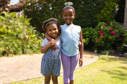 Portrait of smiling african american girl standing with arm around little sister at backyard