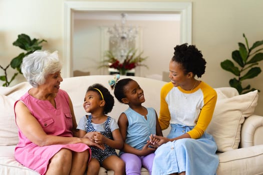 African american grandmother, mother and two granddaughters smiling looking at each other at home