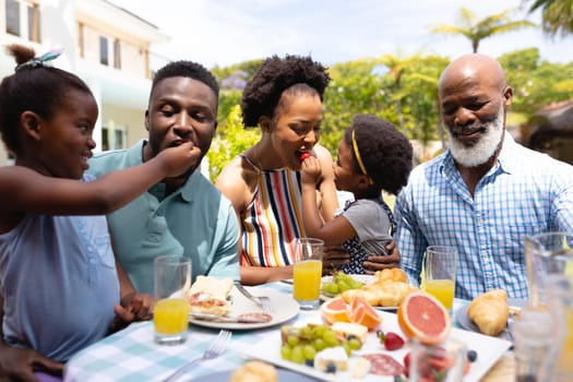 African american girls feeding parents at dining table in backyard during brunch