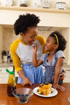 African american daughter feeding berries to her mother in the kitchen at home