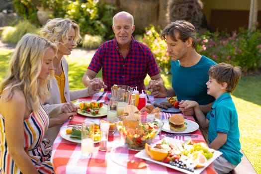 Caucasian three generational family praying before eating lunch in the garden
