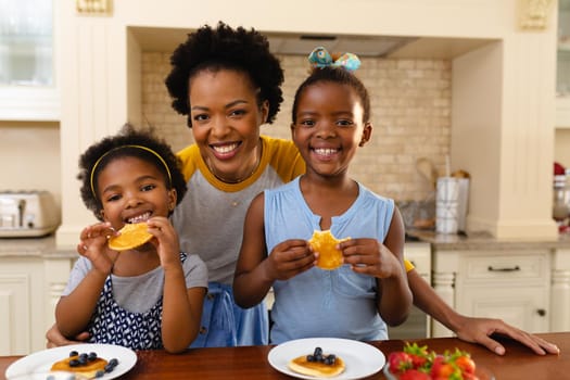 Portrait of african american mother and her two daughters having breakfast in kitchen at home