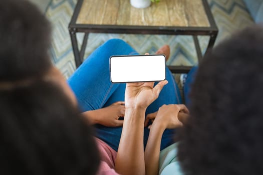 Mother and daughter using smart phone while sitting on sofa at home, copy space