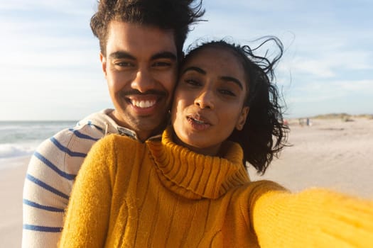 Portrait of smiling young biracial woman taking selfie with boyfriend at beach on sunny day
