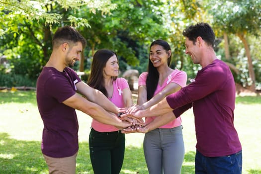 Cheerful multiracial men and women stacking hands during breast cancer awareness campaign