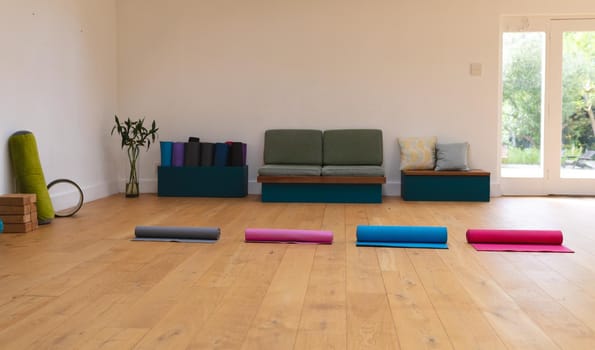 Colorful rolled up exercise mats arranged side by side on hardwood floor in yoga studio, copy space