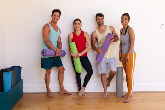 Portrait of smiling multiracial men and women with yoga mats against wall in yoga studio. healthy lifestyle and fitness.