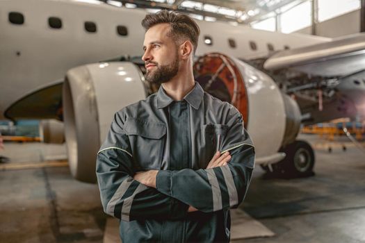Bearded man airline mechanic standing near airplane in hangar