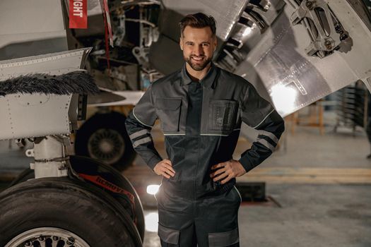 Joyful male mechanic standing near airplane in hangar