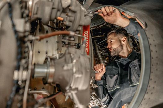 Bearded man mechanic repairing aircraft in hangar