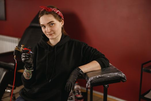 Woman tattoo artist in gloves holding tattooer machine