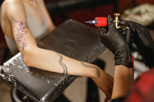 Photo of tattoo master hands in black gloves turning on tattoo machine