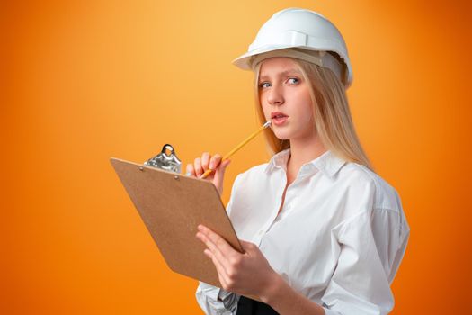 Teen girl in hardhat and clipboard against orange background