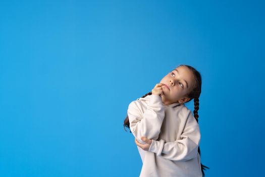 Little girl thinking and looking up over blue background