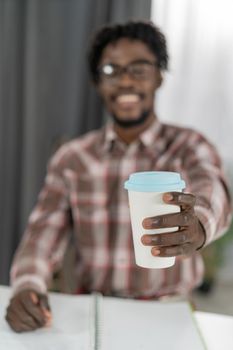 Selective focus on African american man hand with cardboard cup or disposable cup for coffee or tea. White disposable cup with blue plastic lead in mans hand. Disposable dishes concept