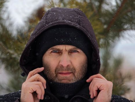 Serious face of a man with a stubble beard and a hooded winter close-up.