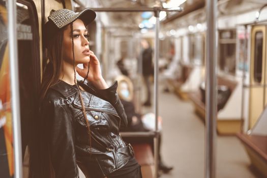 Pretty Caucasian Woman in Leather Jacket and Stylish Cap Leaning Back against the Underground Train Door. Beautiful Face. Close-up Portrait. Toned picture.