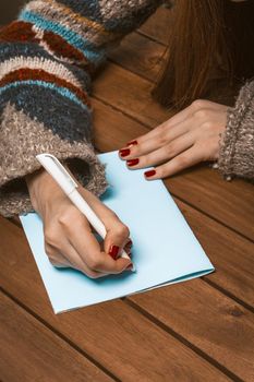 Woman Hands with Red Manicure on a Wooden Table Write a Greeting Card with a Pen. Woman Fill in a Letter on a Piece of Blue Paper. Blank Sheet. Close-up