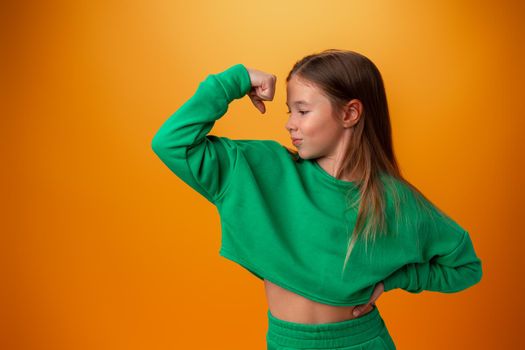 Teen girl showing off muscles biceps against orange background