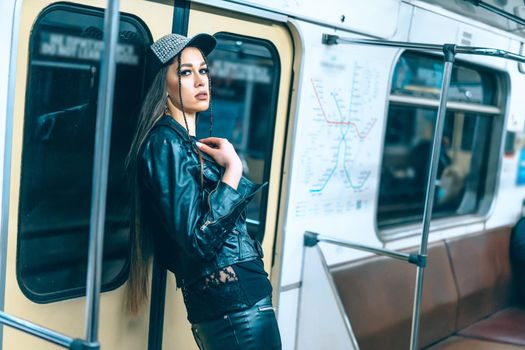 Sexy Woman in Stylish Clothes with Long Brown Hair Stands by Back at the Door in a Train Car. Glamorous Female in Empty Underground Train. Close-up