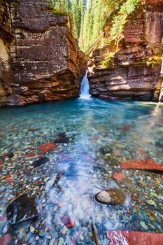 Waterfall cutting through steep cliffs into pristine blue water with colorful rocks