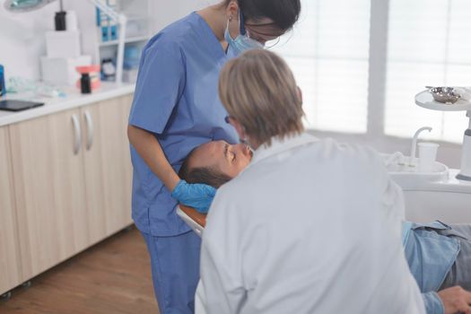 Clinical orthodontist team with face mask examining patient mouth