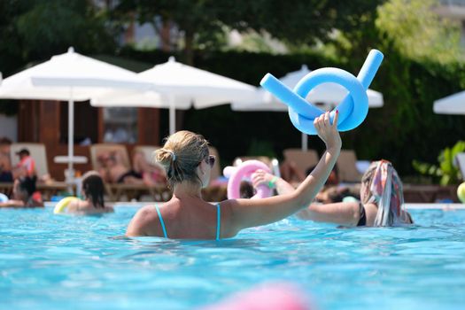 Female instructor holding blue noodle at sports workout in swimming pool