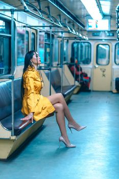 Charming Lady in a Cute Sexy Yellow Dress with Delightful Slender Legs Sitting Inside the Empty Underground Train. Full Size Profile of Nice Woman in Yellow Coat in the Train. Close-up