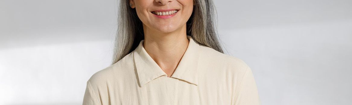 Portrait of pretty grey haired woman in beige blouse on light background