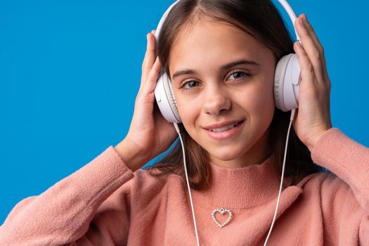 Schoolgirl with headphones listening to music against blue background