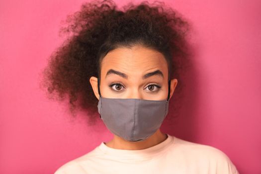 Recognize emotions in a reusable mask during quarantine African American girl in peachy t-shirt, to prevent others from corona COVID-19 and SARS cov 2 infection isolated on pink background