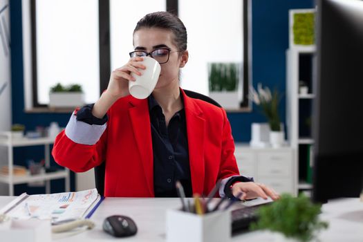 Employee with glasses at startup desk drinking from white cup.