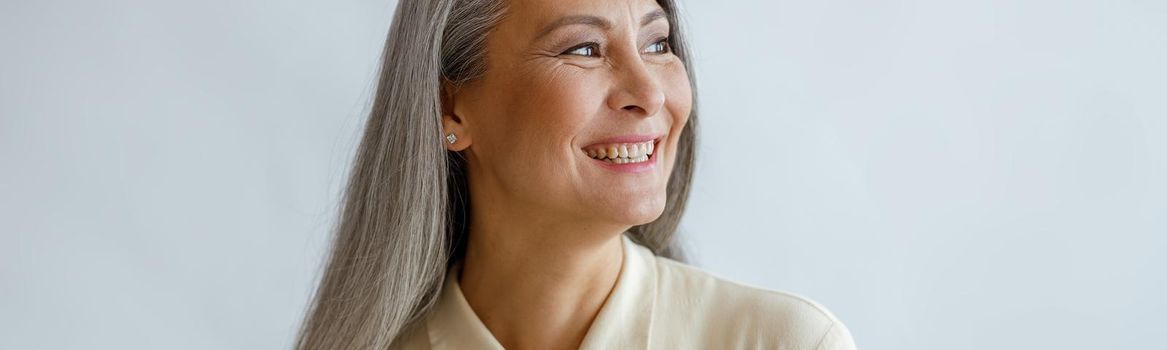 Joyful lmiddle aged lady wearing beige blouse stands on light background