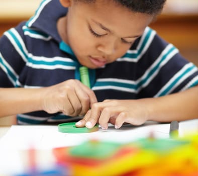 Its creative time. Pre-school african american boy concentrating on his drawings with his crayons and shapes.