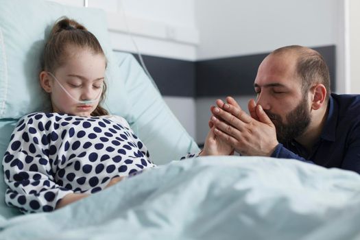 Attentive sad worried father holding unwell hospitalized daughter hand
