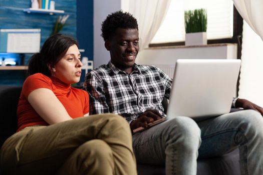 Interracial relaxed couple looking at laptop screen