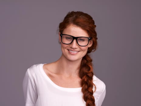 Casual and confident. Studio shot of an attractive young redheaded woman against a grey background.