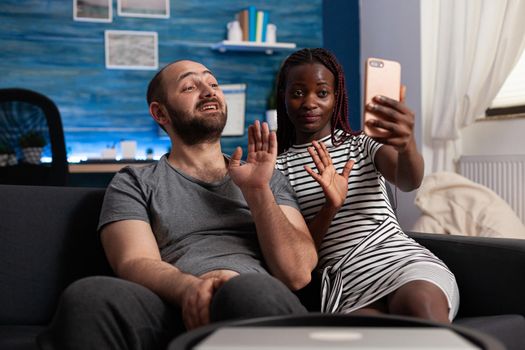 Happy interracial married couple waving at modern phone